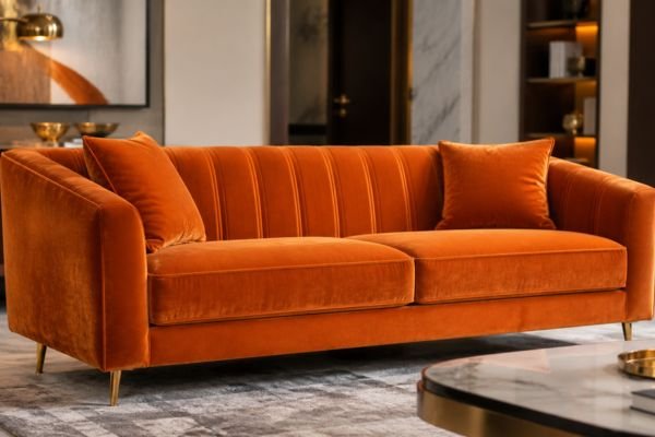 Modern luxury orange velvet sofa with gold legs in a sophisticated living room setting.
