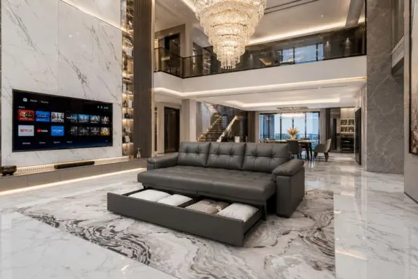 Charcoal gray tufted sleeper couch with open storage drawers in a marble penthouse.