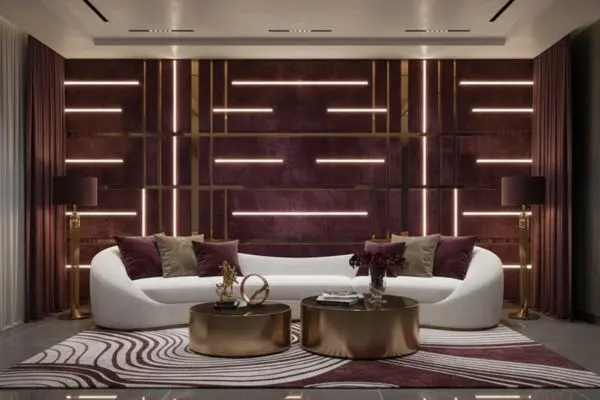 Elegant white curved lounge couch in a deep burgundy and brass maximalist luxury interior room with modern linear lighting.