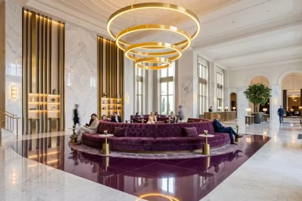 Massive deep plum purple velvet island seating in a grand hotel lobby with a glowing circular gold chandelier