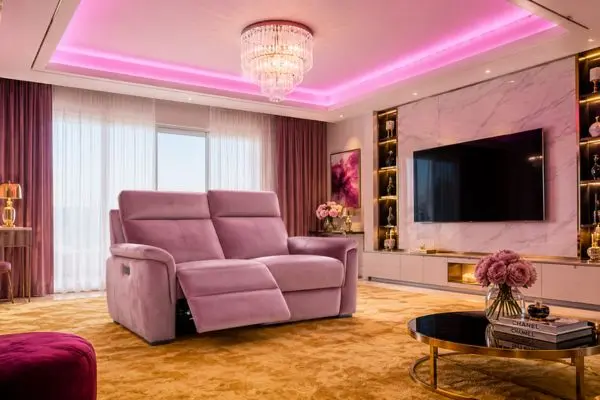 Luxury pastel pink velvet 2 seater recliner sofa under vibrant ambient LED ceiling lights.