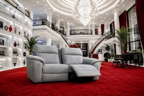 Luxury grey 2 seater recliner sofa on a plush royal red carpet inside a grand mansion.