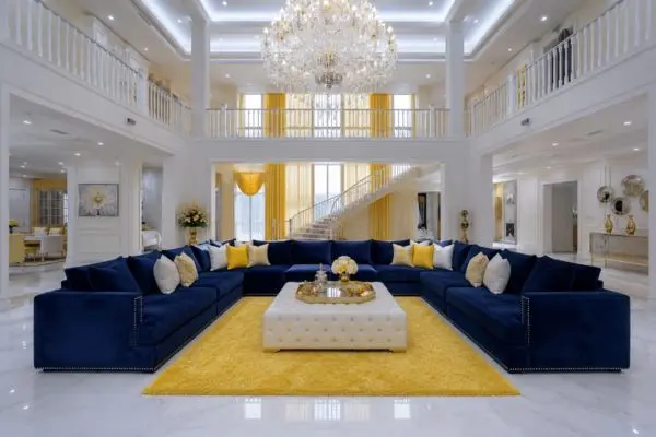 Deep blue velvet curved seating arranged on a bright yellow rug under a grand crystal chandelier