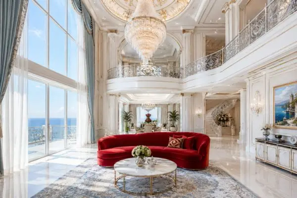 An elegant medium curved crimson seating piece on a blue and cream traditional rug facing an ocean view.
