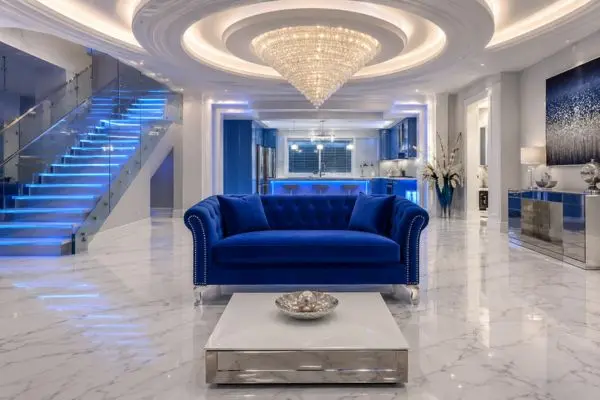 Modern royal blue two seater velvet couch centered in a luxury open layout with stair lights.