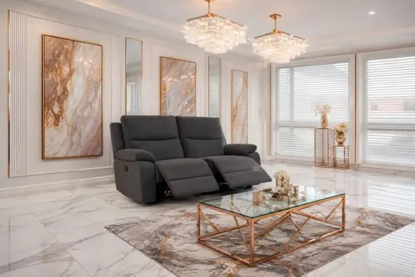 A charcoal grey fabric small reclining sofa loveseat with extended footrests in a luxury white marble room.