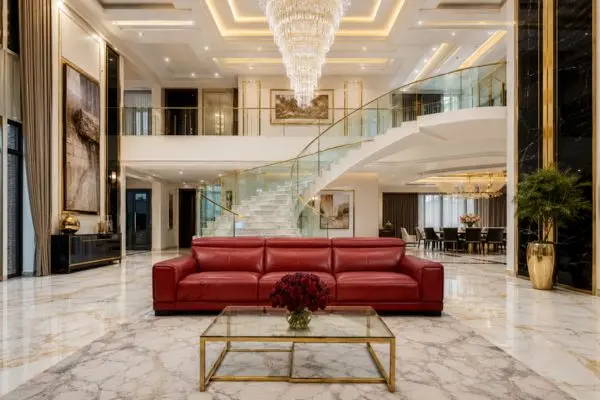 Modern red leather sofa in a luxury double height mansion hall with a grand staircase.