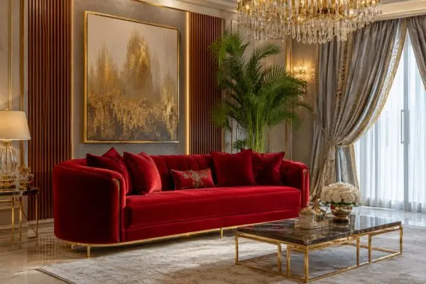 Luxurious plush crimson couch placed inside an opulent grey and gold decorated living room space.