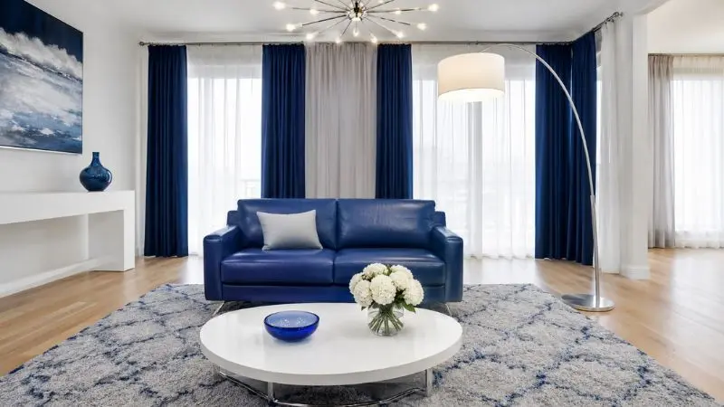 A compact small blue leather sofa placed in a modern white living room setup.